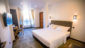 A hotel room with a large bed, a desk, a chair, a television, and a window with curtains. - Huddle (Nuwara Eliya)