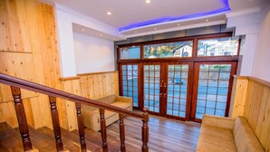 A wooden staircase with a wooden handrail, a beige sofa, and a large glass door with a view of the outside. - Huddle (Nuwara Eliya)