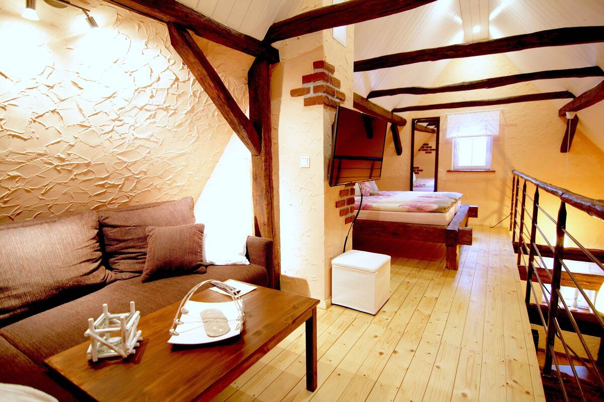 A cozy room with a wooden floor, a bed with a white headboard, a small white table, and a brown sofa.