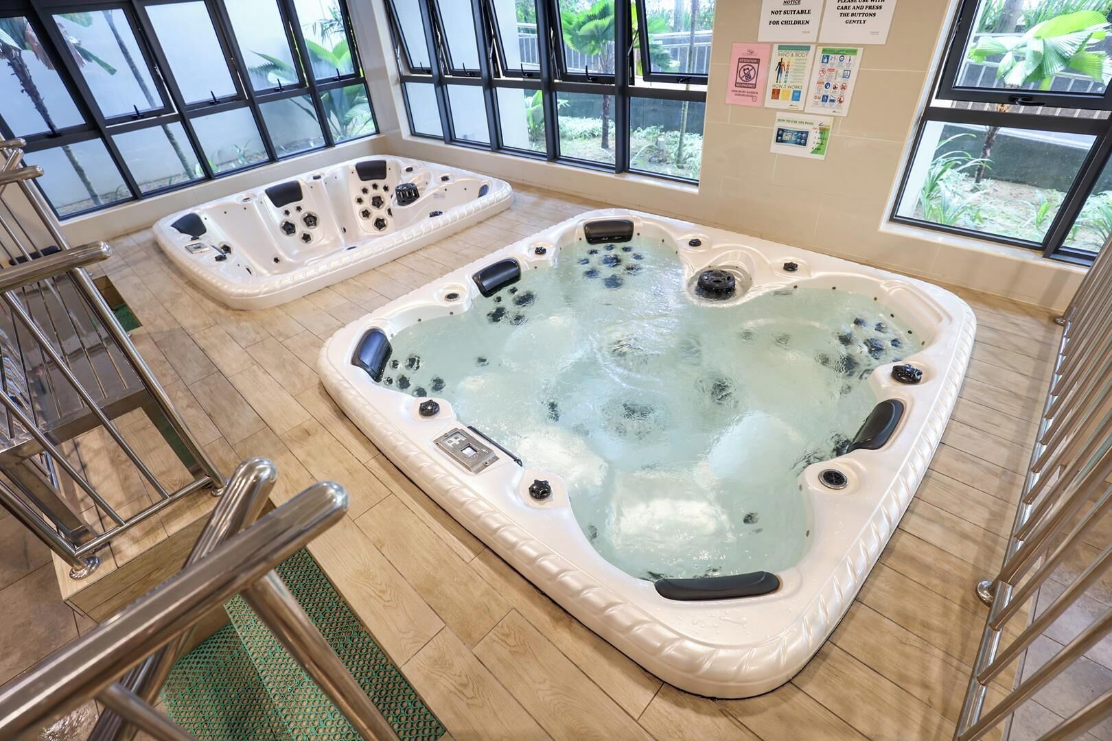 A large indoor hot tub with multiple jets, surrounded by large windows and a wooden floor.