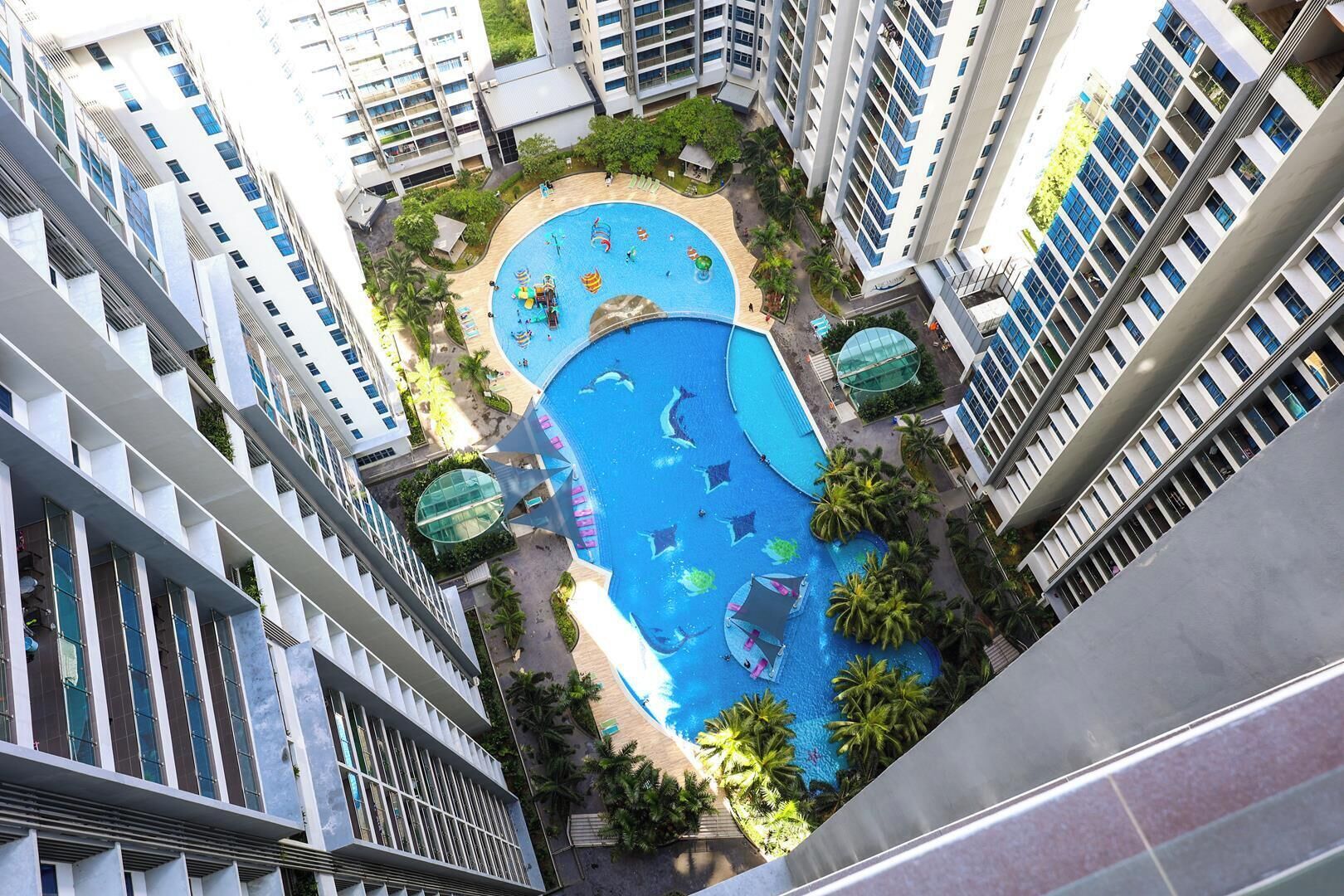 Un edificio de gran altura con una piscina central rodeada de palmeras y una zona de juegos para niños.