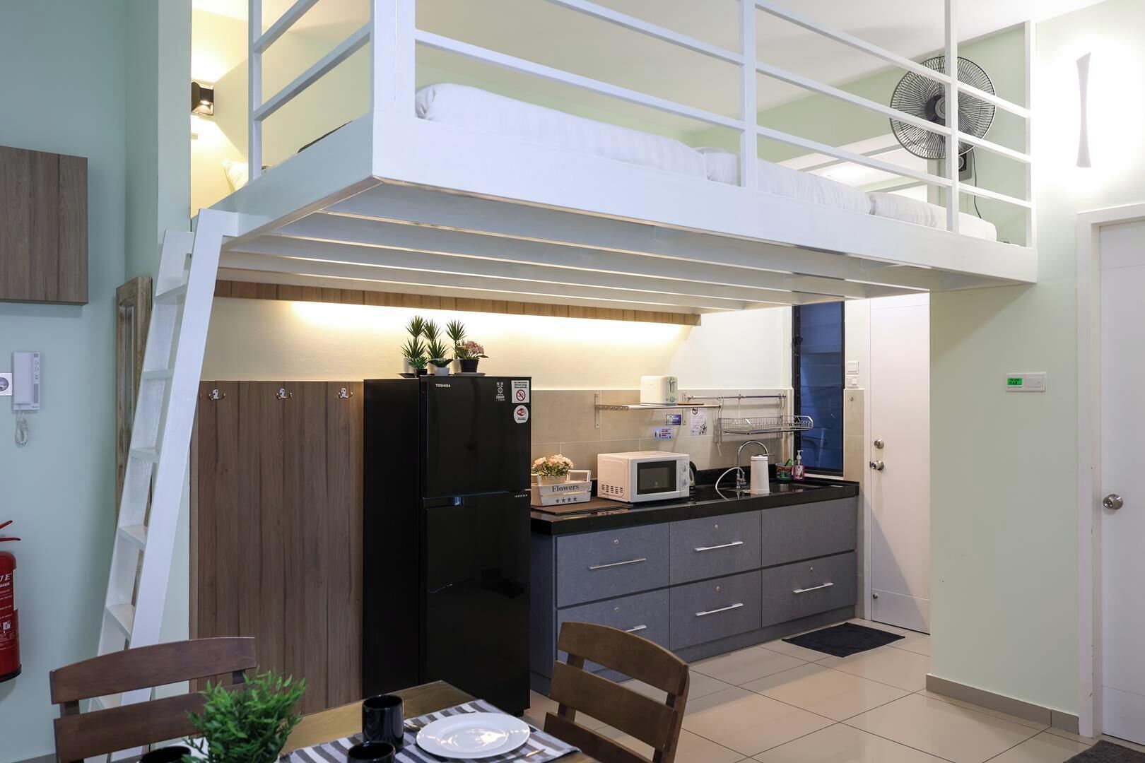 Cocina compacta con refrigerador, microondas y un pequeño comedor con mesa y sillas.