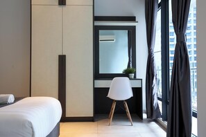 Moderni hotellihuone, jossa on sänky, työpöytä, tuoli, suuri peili ja ikkunasta avautuva näkymä kaupunkiin.