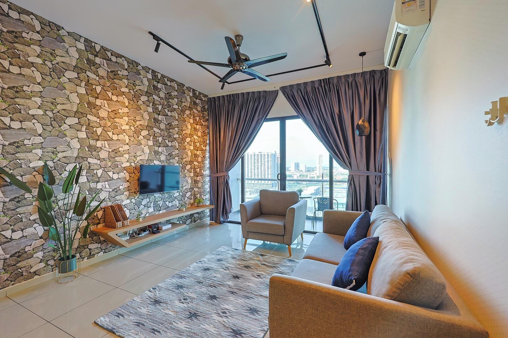 A living room with a stone wall, a flat-screen TV, a ceiling fan, and a sofa with cushions.