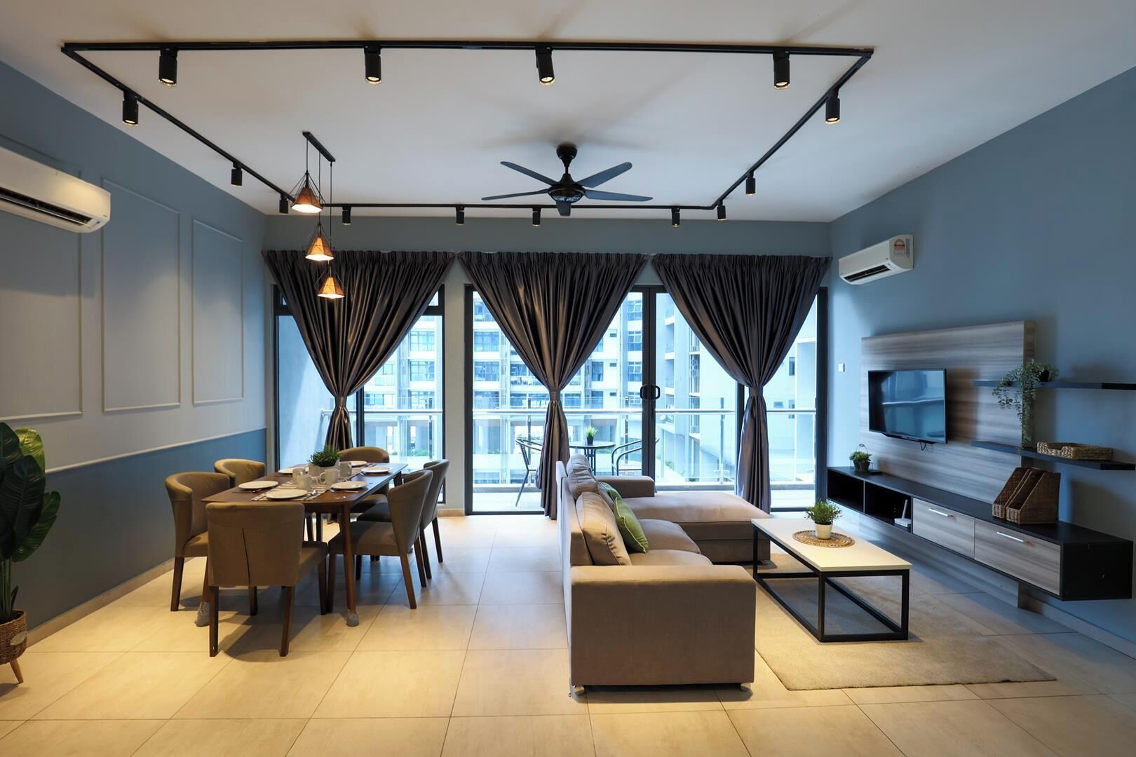 Una sala de estar moderna con comedor, ventanas grandes con cortinas, ventilador de techo y televisor de pantalla plana montado en la pared.