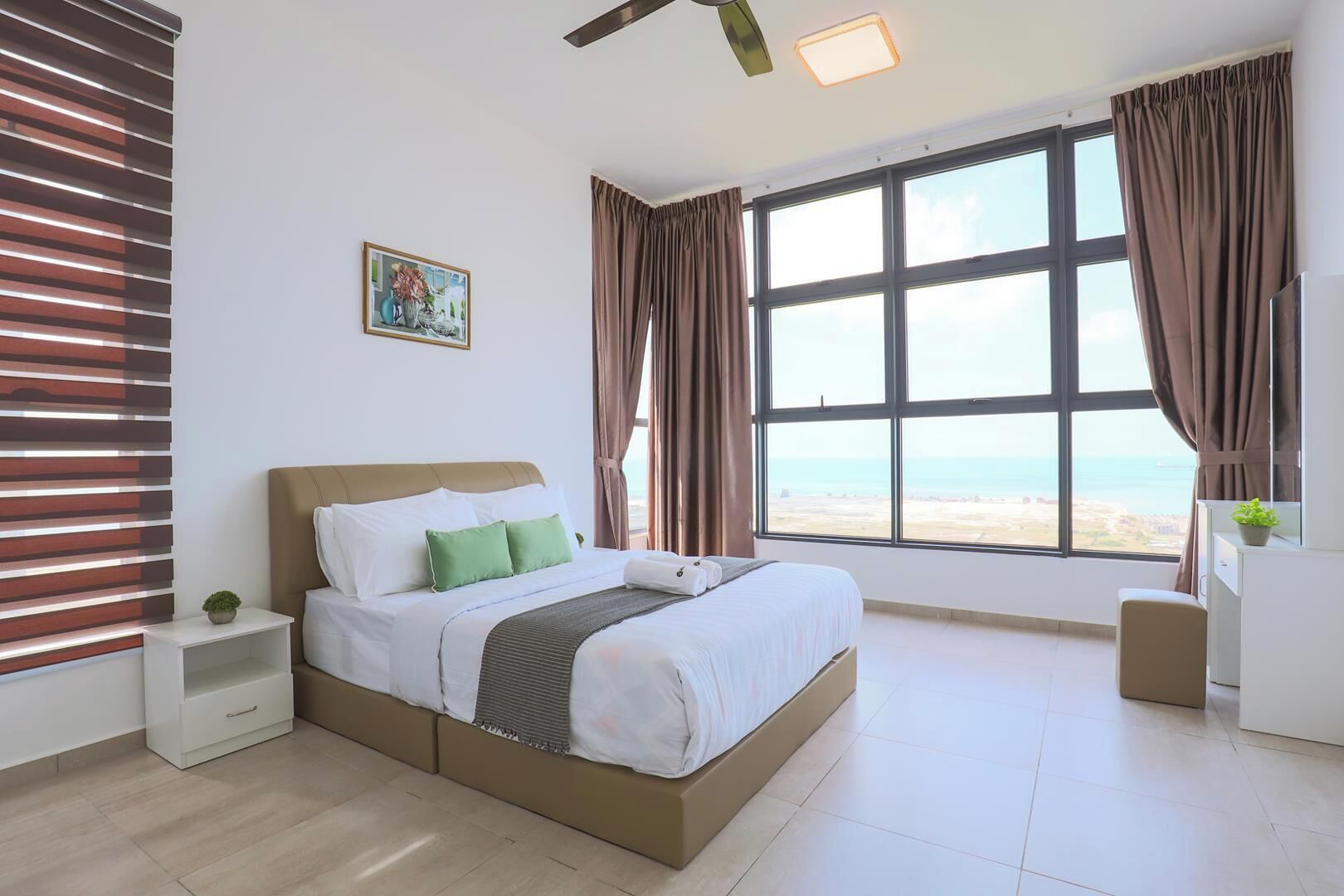 Habitación de hotel con un ventanal grande, una cama con ropa de cama blanca, una mesita de noche y una planta pequeña.
