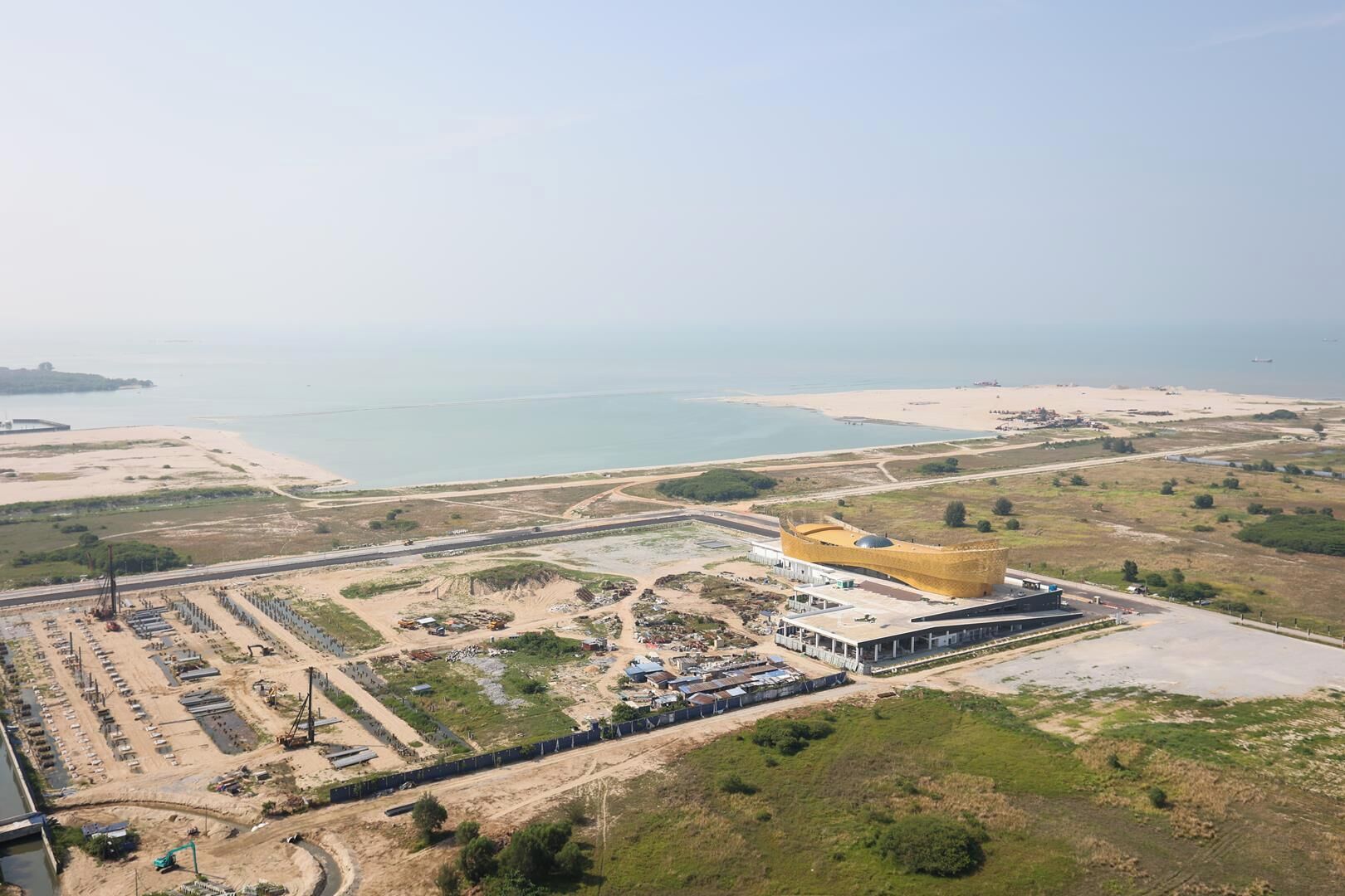 An aerial view of a coastal area with a distinctive yellow building, a sandy beach, and a large body of water.