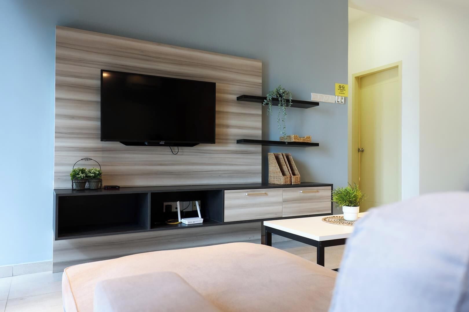 A modern living room with a flat-screen TV mounted on a wooden wall, a sofa, a coffee table, and a small plant on a shelf.