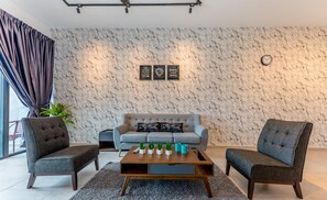 Un salón moderno con pared de diseño de mármol, un sofá gris, dos sillones, una mesa de centro con objetos decorativos y un reloj en la pared.
