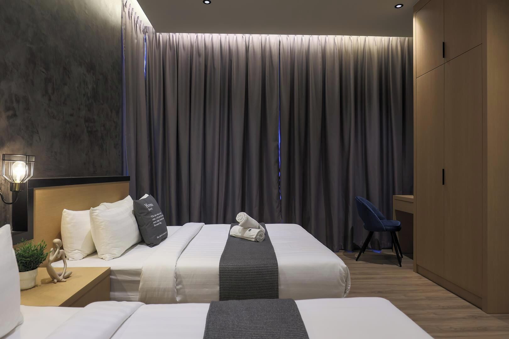 A hotel room with two beds, a nightstand, a lamp, a chair, and a large window with curtains.