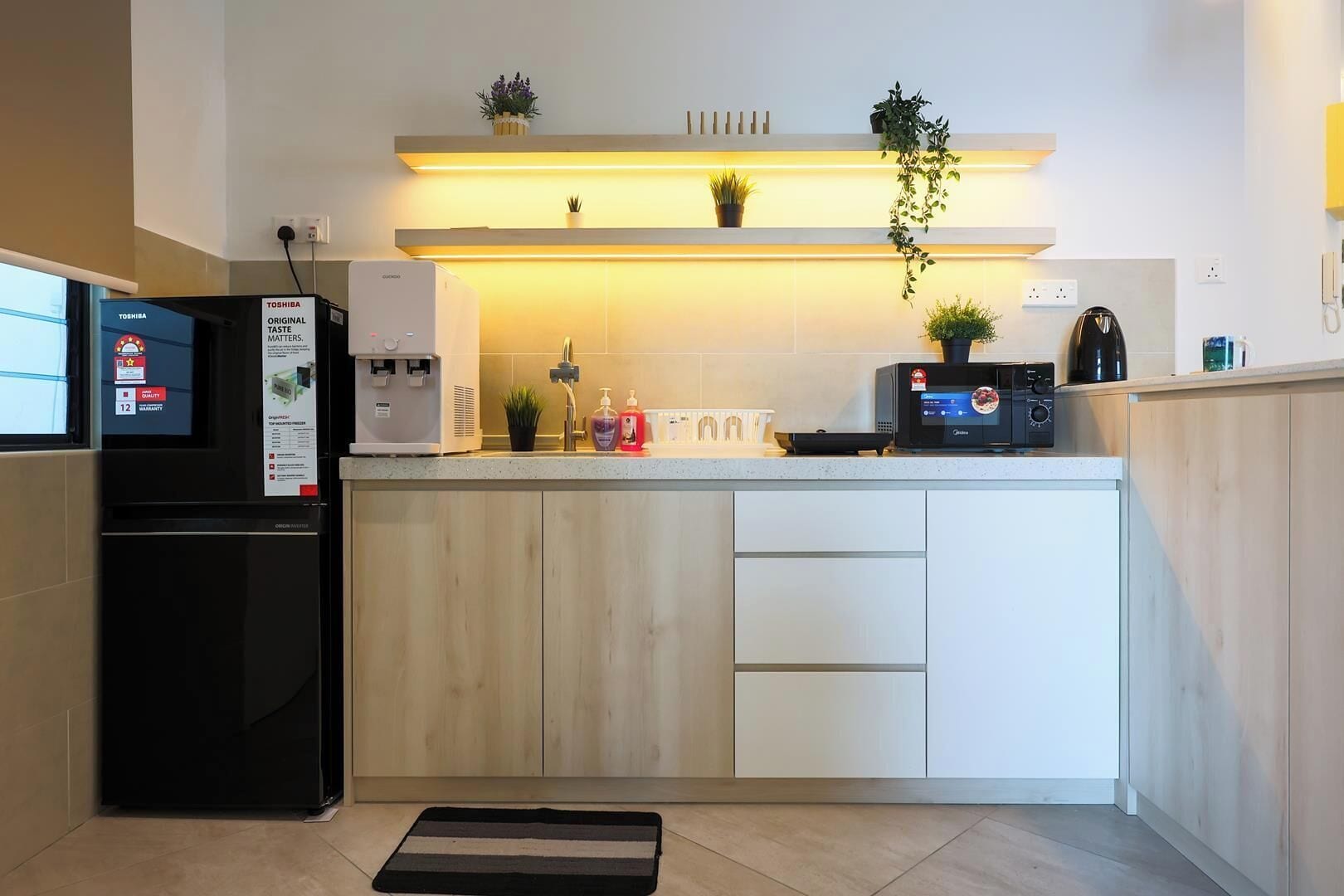 A compact kitchen with a refrigerator, a coffee maker, a microwave, and a small countertop with a plant.