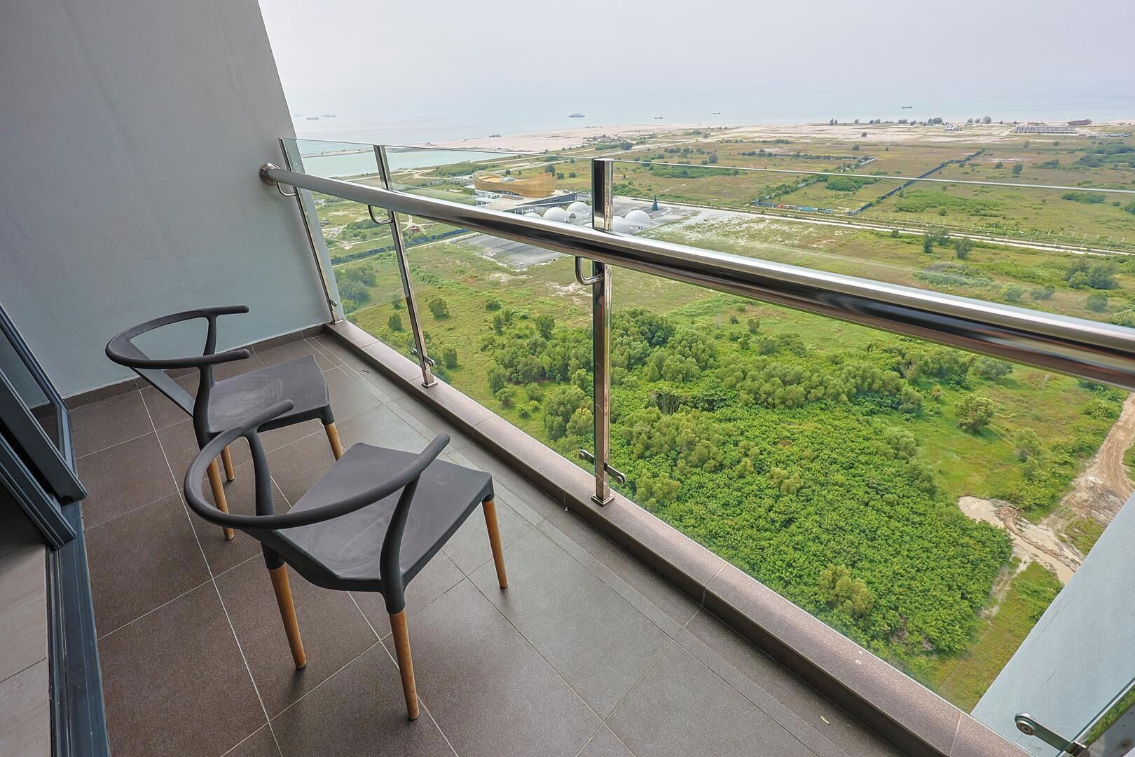 A balcony with two chairs and a view of a green landscape and a distant body of water.