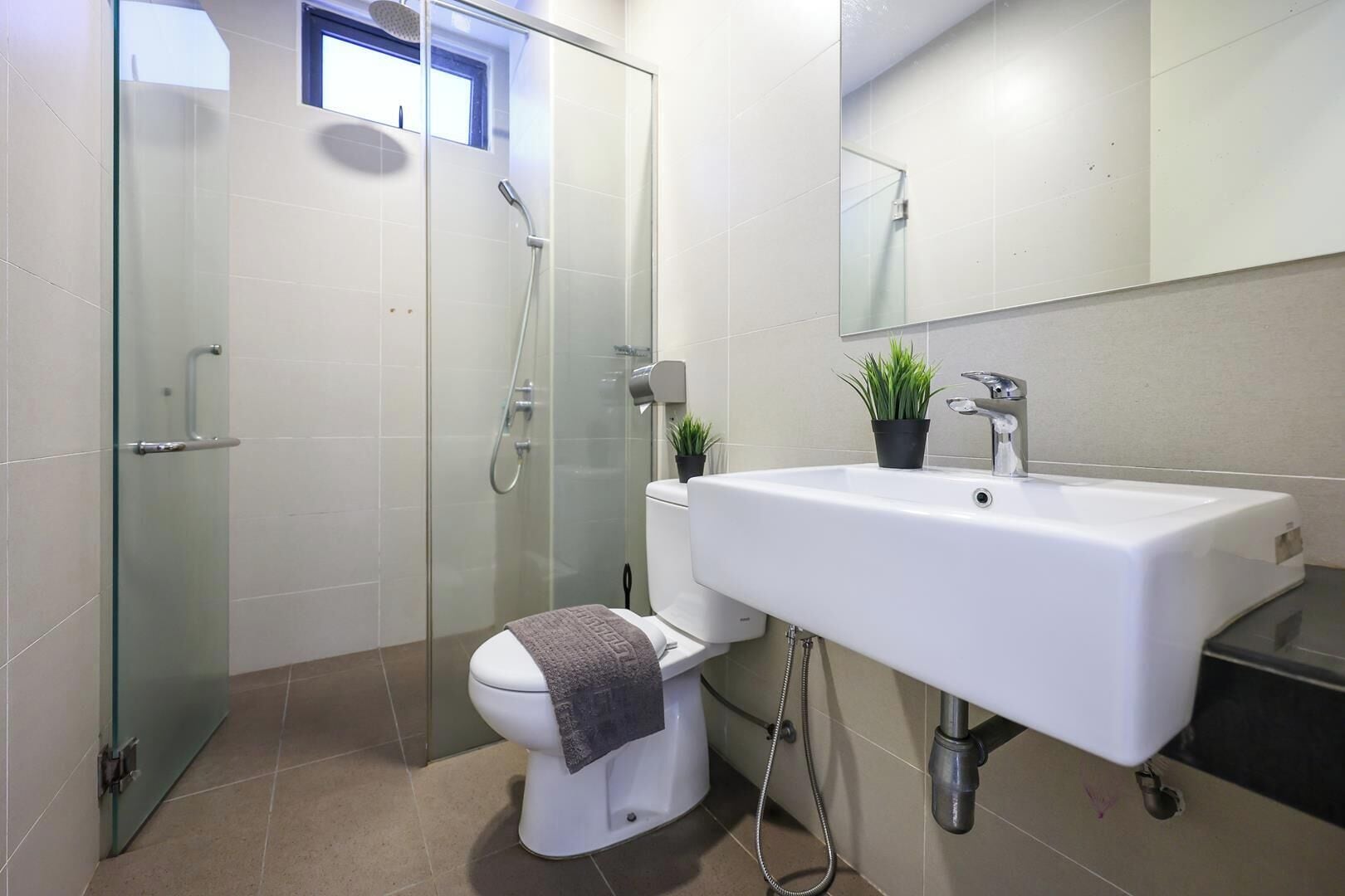 A modern bathroom with a glass-enclosed shower, a white toilet, and a sink with a mirror above it.