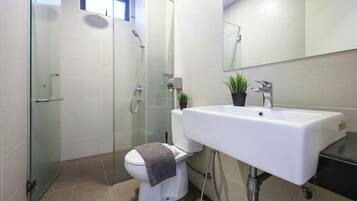 A modern bathroom with a glass-enclosed shower, a white toilet, and a sink with a mirror above it.