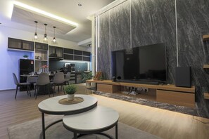 Un salon moderne doté d’un grand téléviseur à écran plat, d’un coin repas avec des chaises et une table, et d’une cuisine équipée d’un réfrigérateur et de placards.