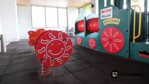 Een speelruimte voor kinderen met een grote rode sculptuur van een lachend gezicht, een bord met welkomstboodschap en trainingsapparatuur.