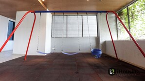 Een ruime kamer met een schommel en een groot raam, met uitzicht op groen.