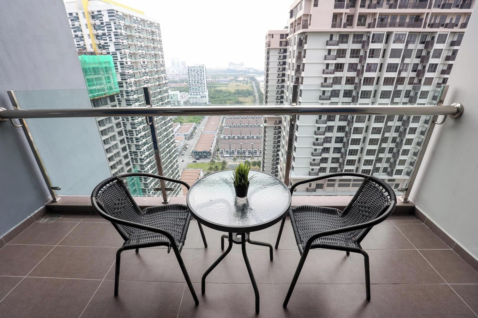 A balcony with two wicker chairs and a small table with a potted plant, overlooking a cityscape with high-rise buildings.