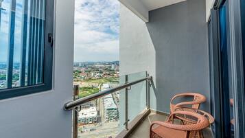 A balcony with a view of a cityscape, a glass railing, and a wicker chair.