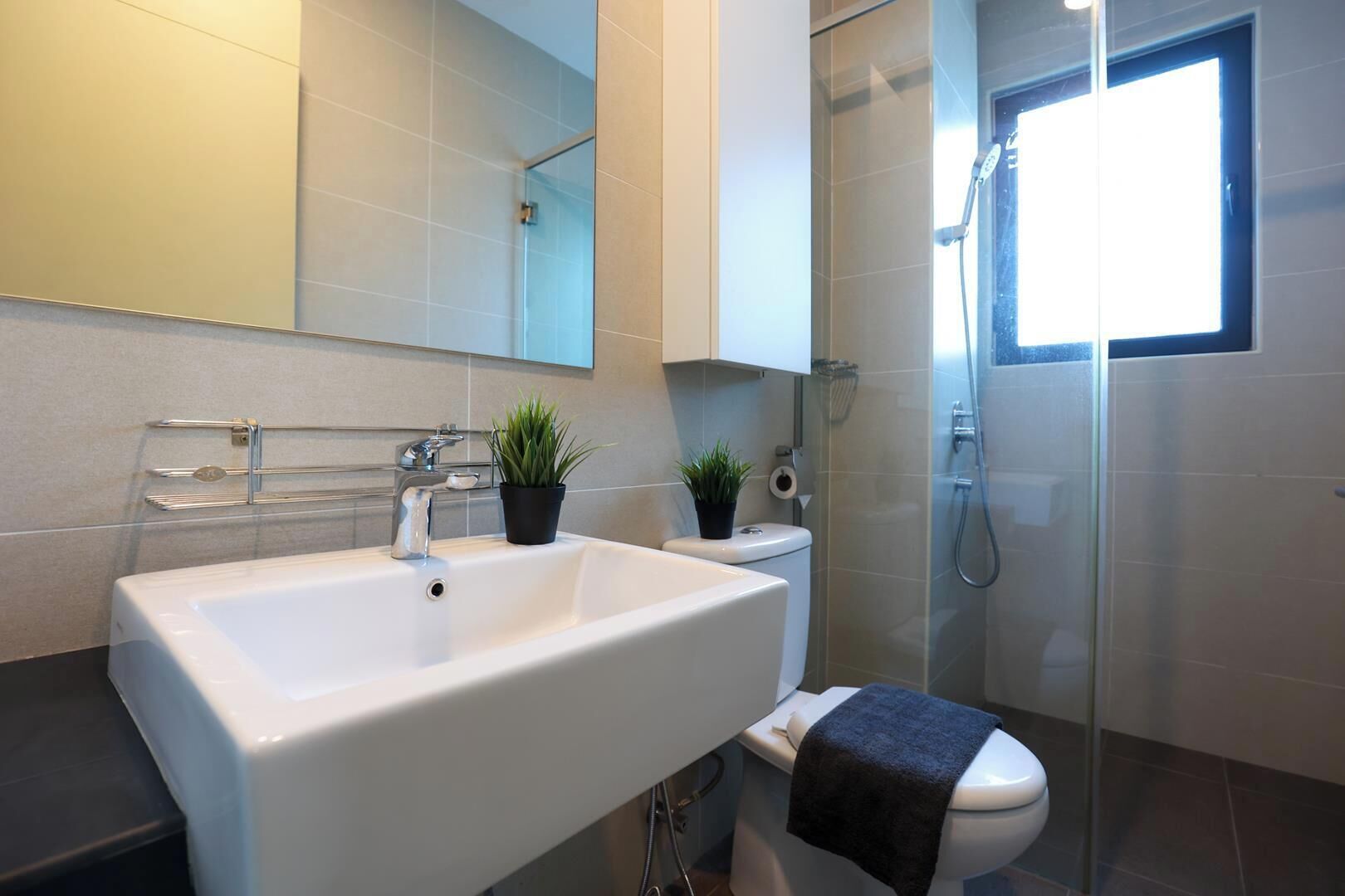 A modern bathroom with a large white sink, a toilet, a glass shower enclosure, and a small window providing natural light.