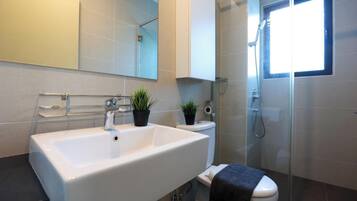 A modern bathroom with a large white sink, a toilet, a glass shower enclosure, and a small window providing natural light.