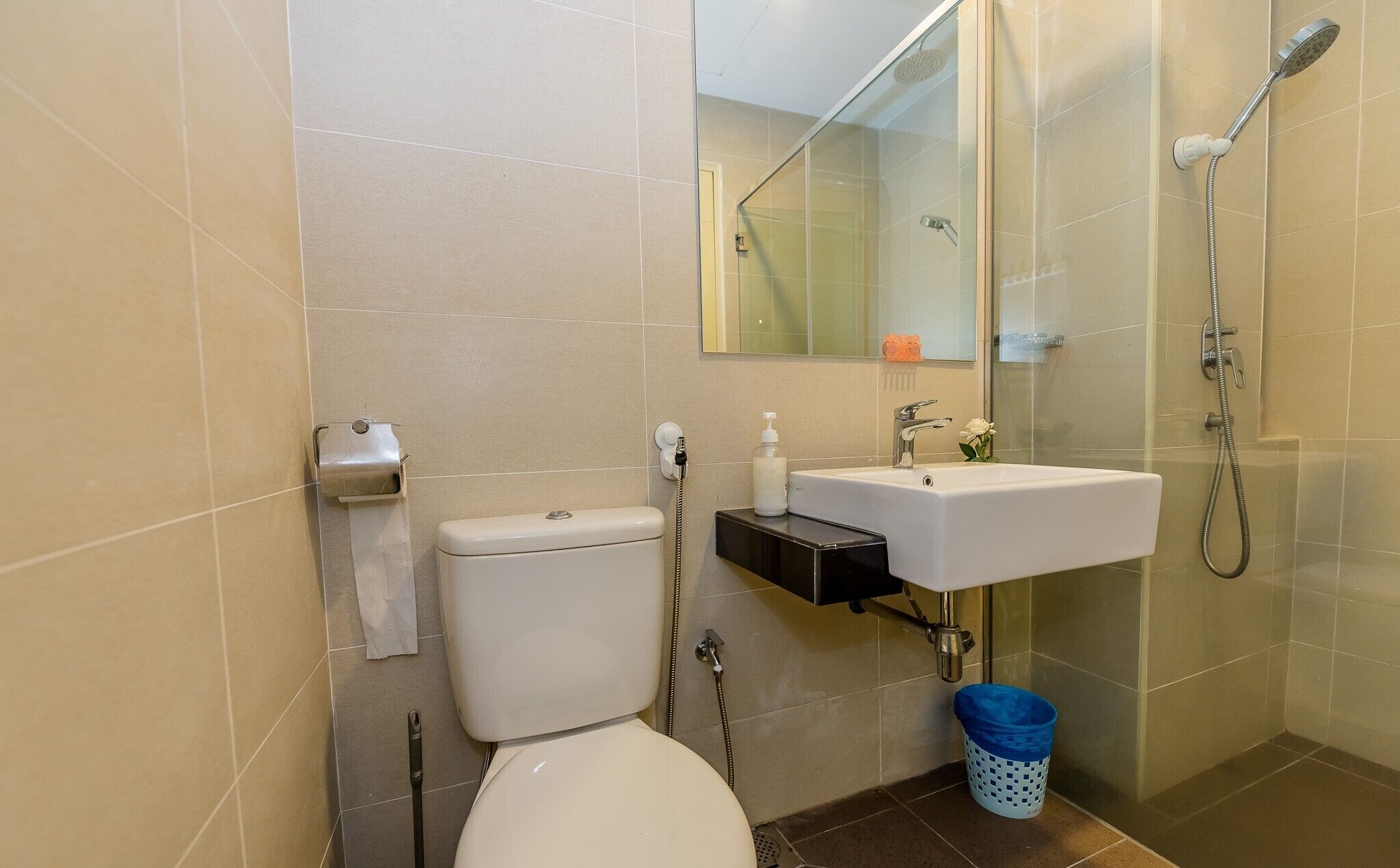 Une salle de bain équipée de toilettes, d’un lavabo, d’une douche et d’une poubelle bleue.