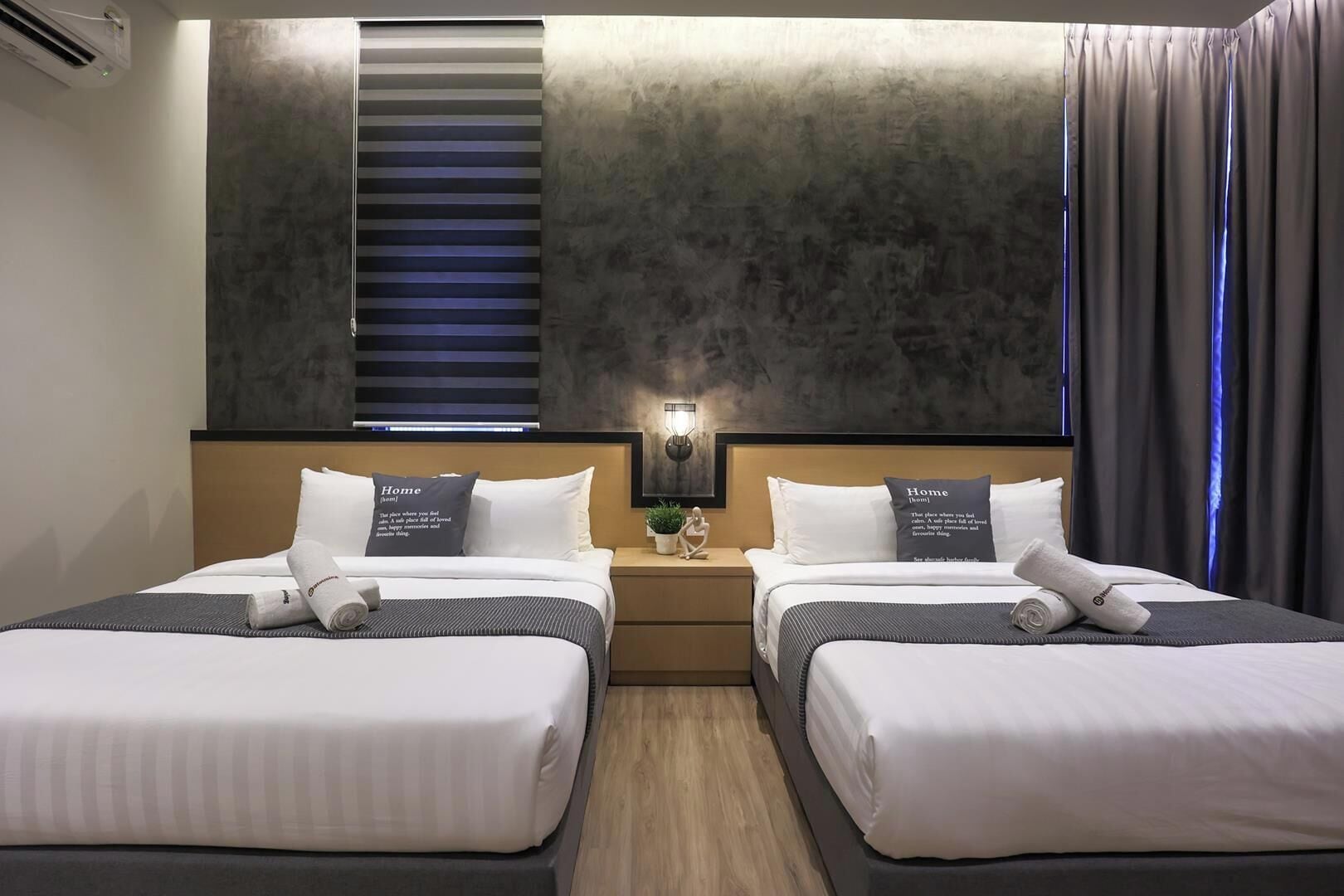 A hotel room with two beds, a nightstand with a lamp, and a window with blinds.