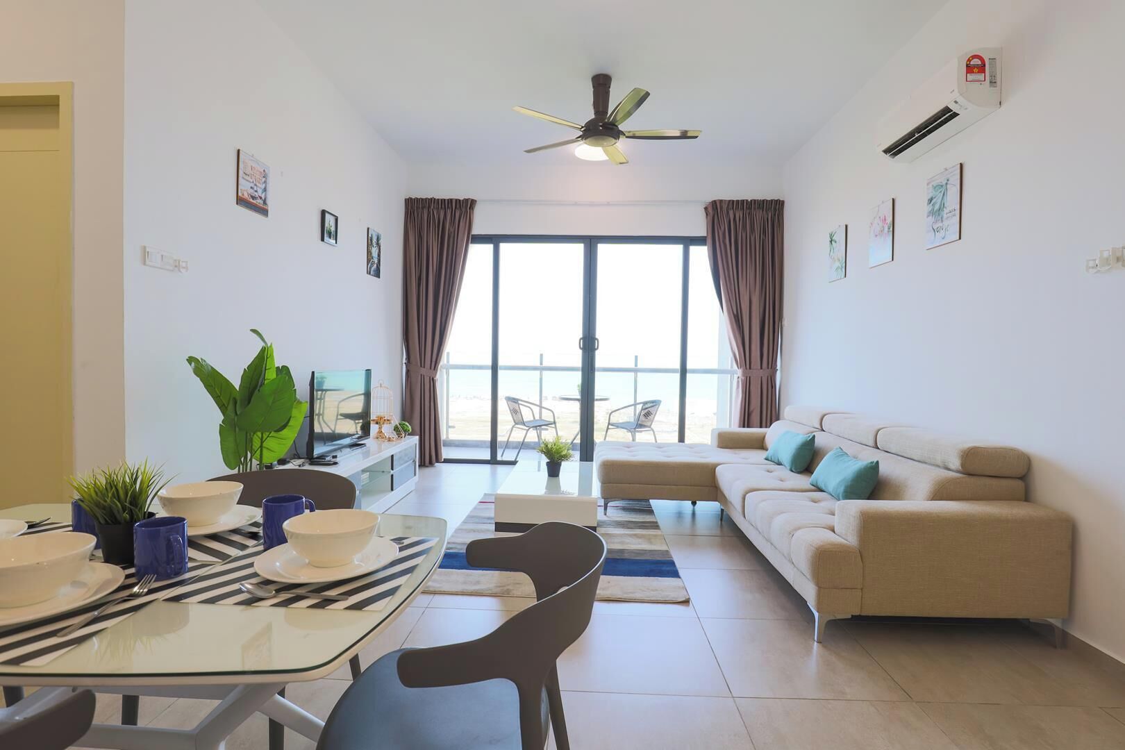 Una sala de estar moderna con sofá, mesa de comedor, sillas, televisión y vistas al exterior.