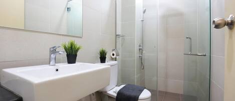A bathroom with a white sink, two potted plants, a toilet, and a glass-enclosed shower.