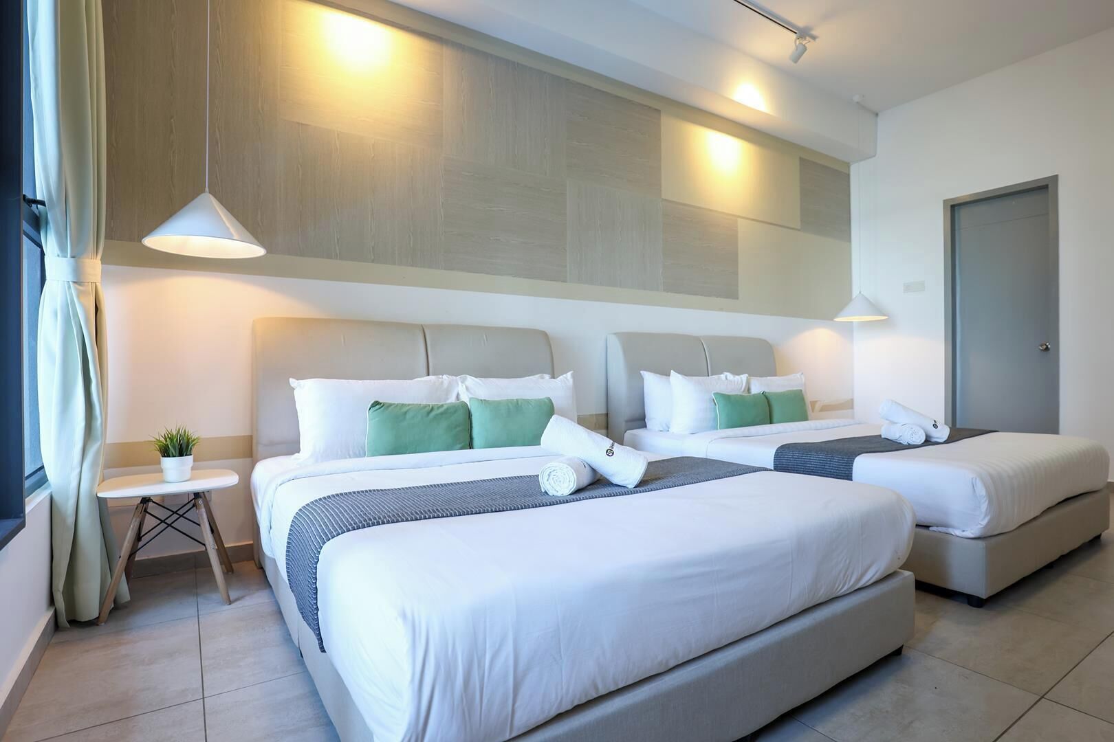 Una habitación de hotel con dos camas, una mesita con una planta y una puerta.