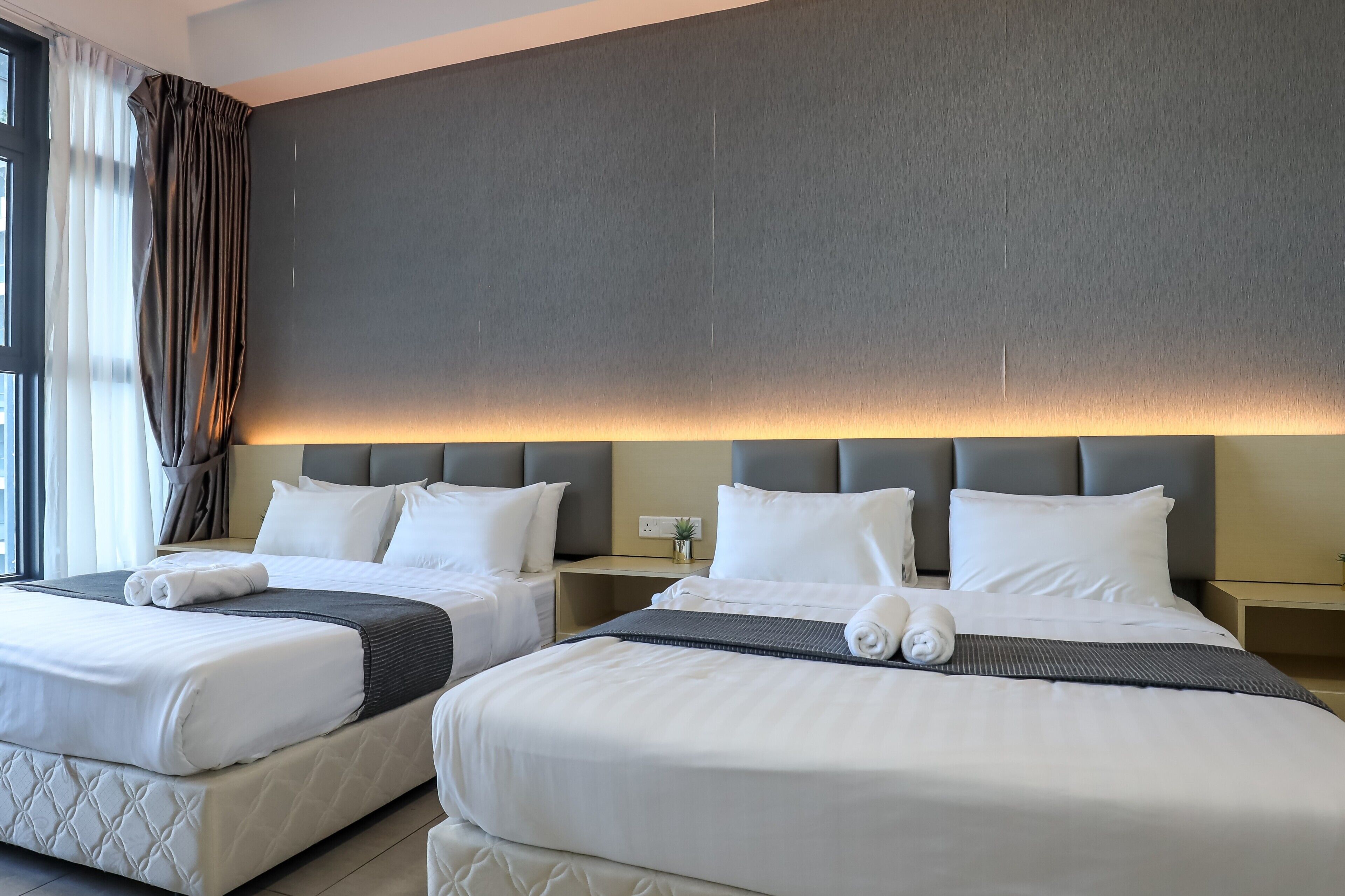 A hotel room with two beds, a large window with curtains, and a wall-mounted light.