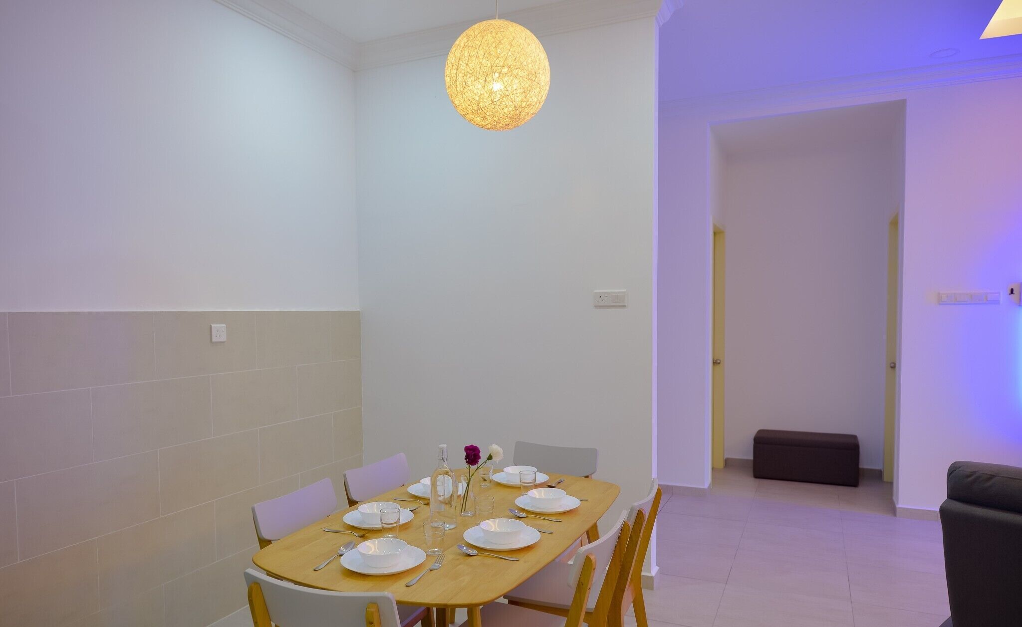 Un coin repas avec une table ronde dressée pour quatre personnes, des chaises blanches et un luminaire suspendu.