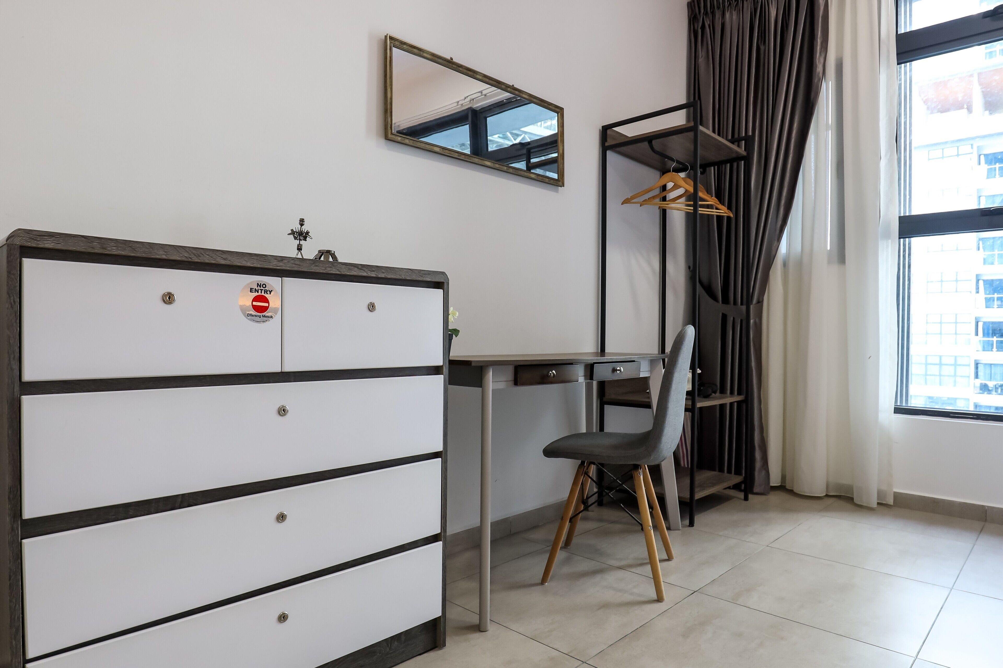 Ein Zimmer mit Schreibtisch, Stuhl, Kleiderschrank und einem Spiegel an der Wand.