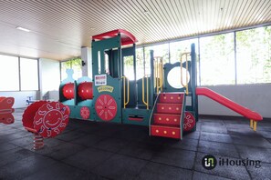 Ein Kinderspielbereich mit Rutsche, Kletterstufen und einer roten und blauen Spielanlage.