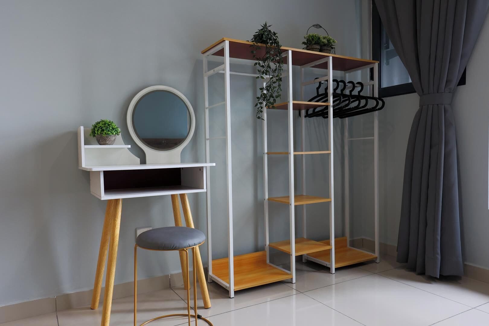 A room with a white vanity, a mirror, a stool, a plant, and a clothing rack.