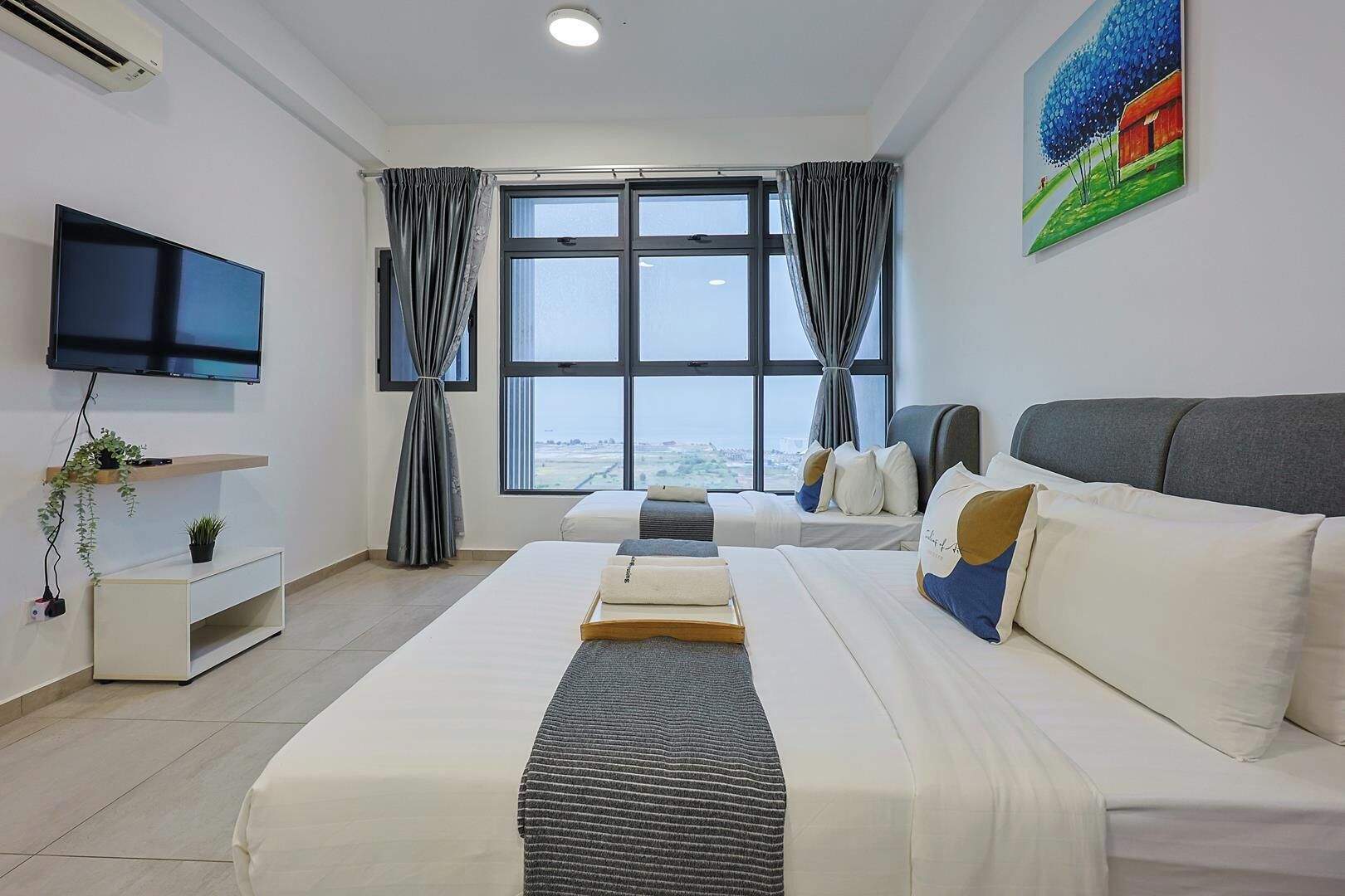 Une chambre d’hôtel avec un lit, une télévision, une fenêtre avec des rideaux et un tableau au mur.