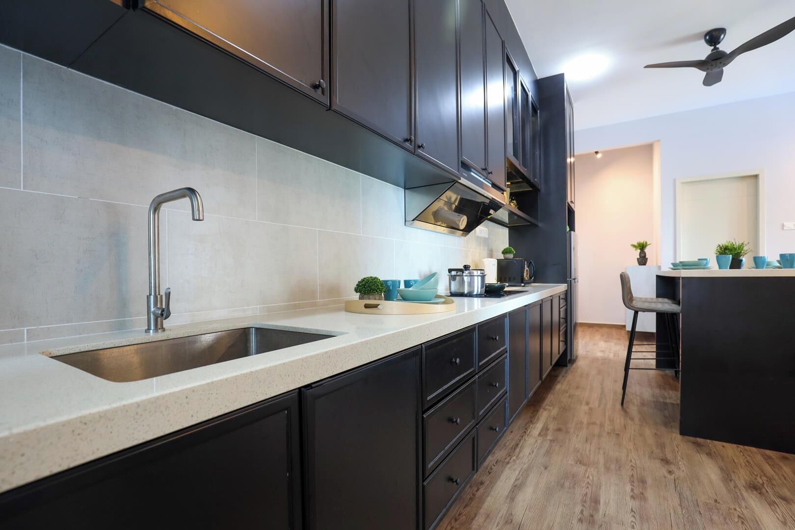 A modern kitchen with dark cabinetry, a stainless steel sink, and a wooden floor.