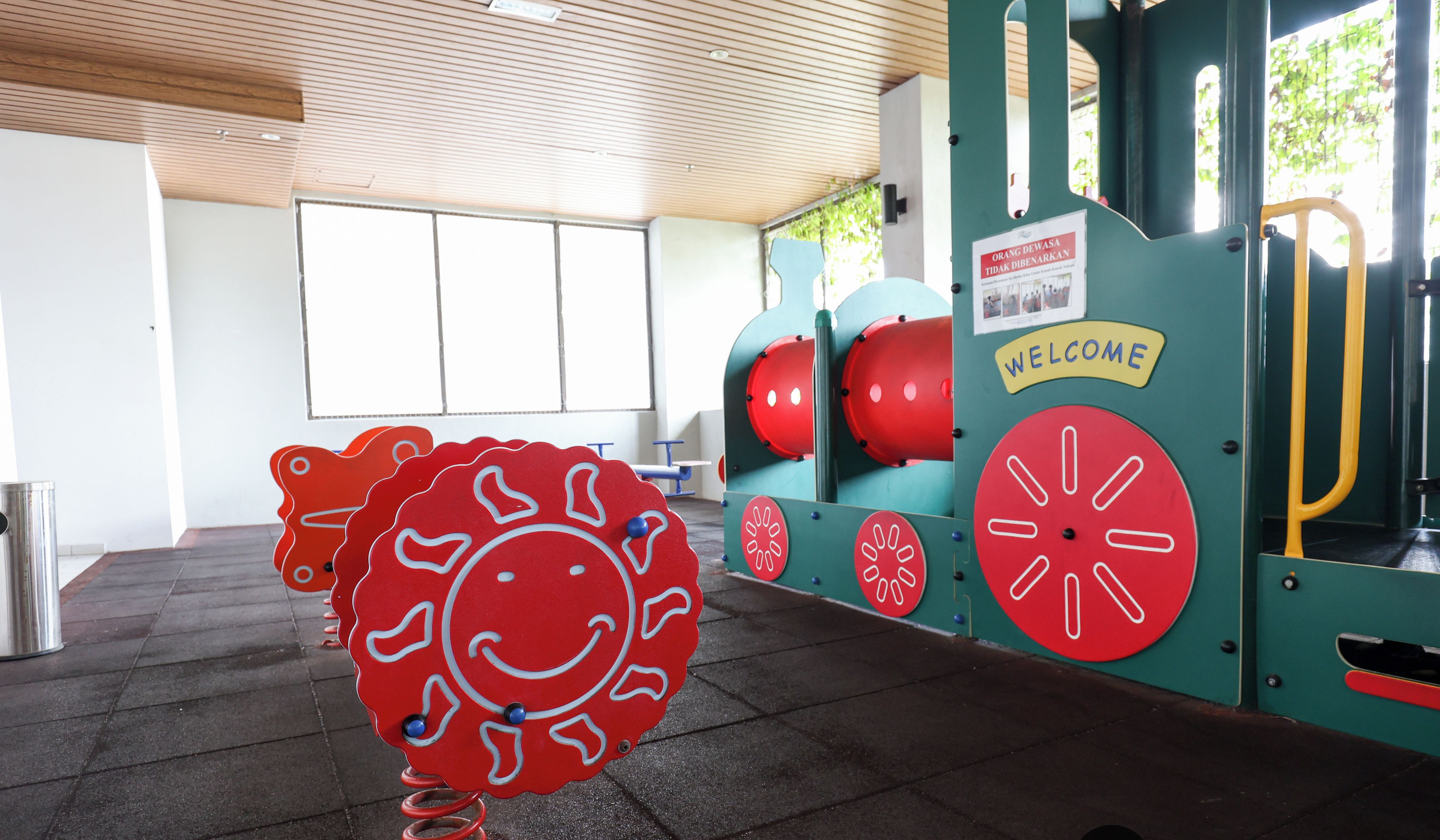 Ein Kinderspielbereich mit einer großen, roten Skulptur im Smiley-Design, einem Willkommensschild und Fitnessgeräten.