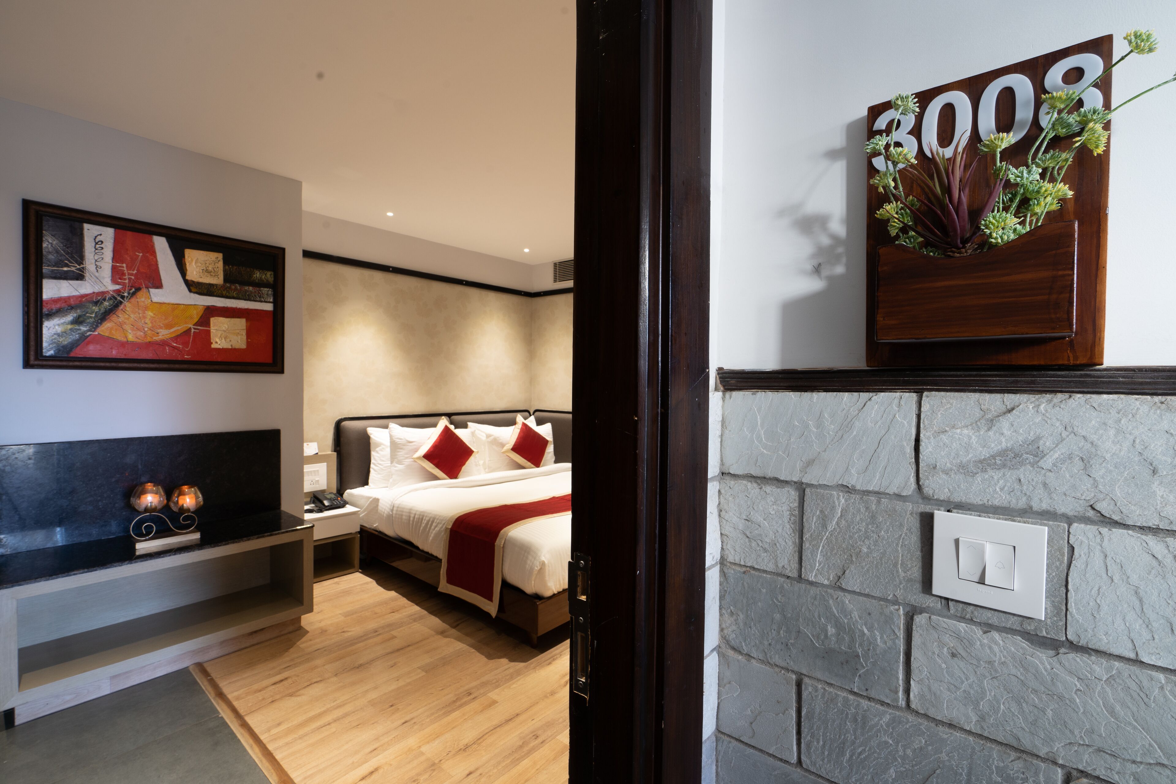 Une chambre d’hôtel moderne, équipée d’un lit, de tables de chevet, d’une œuvre d’art accrochée au mur et d’un mur en pierre avec un interrupteur.