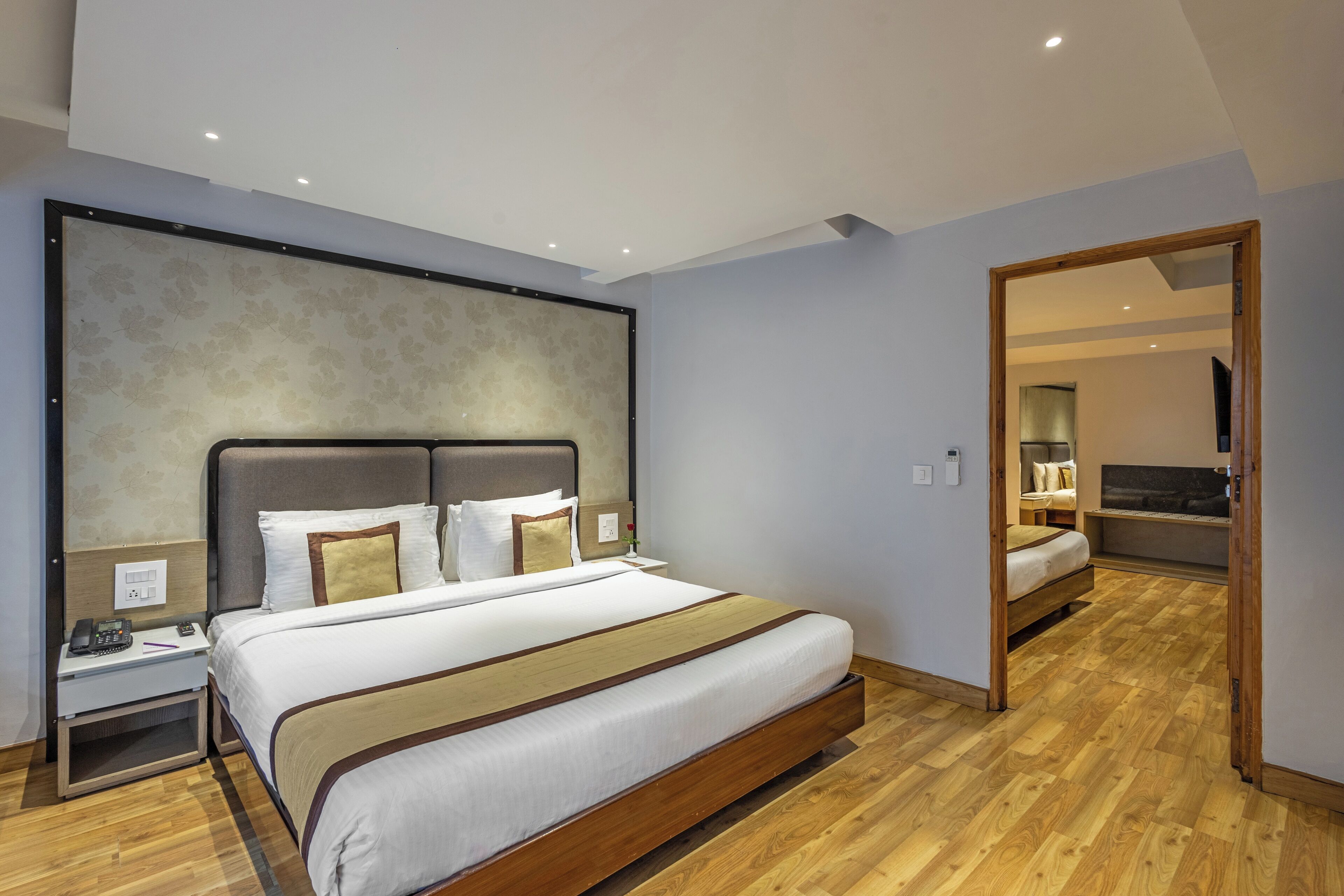 A modern hotel room with a large bed, wooden flooring, a nightstand with a phone, and a mirror.