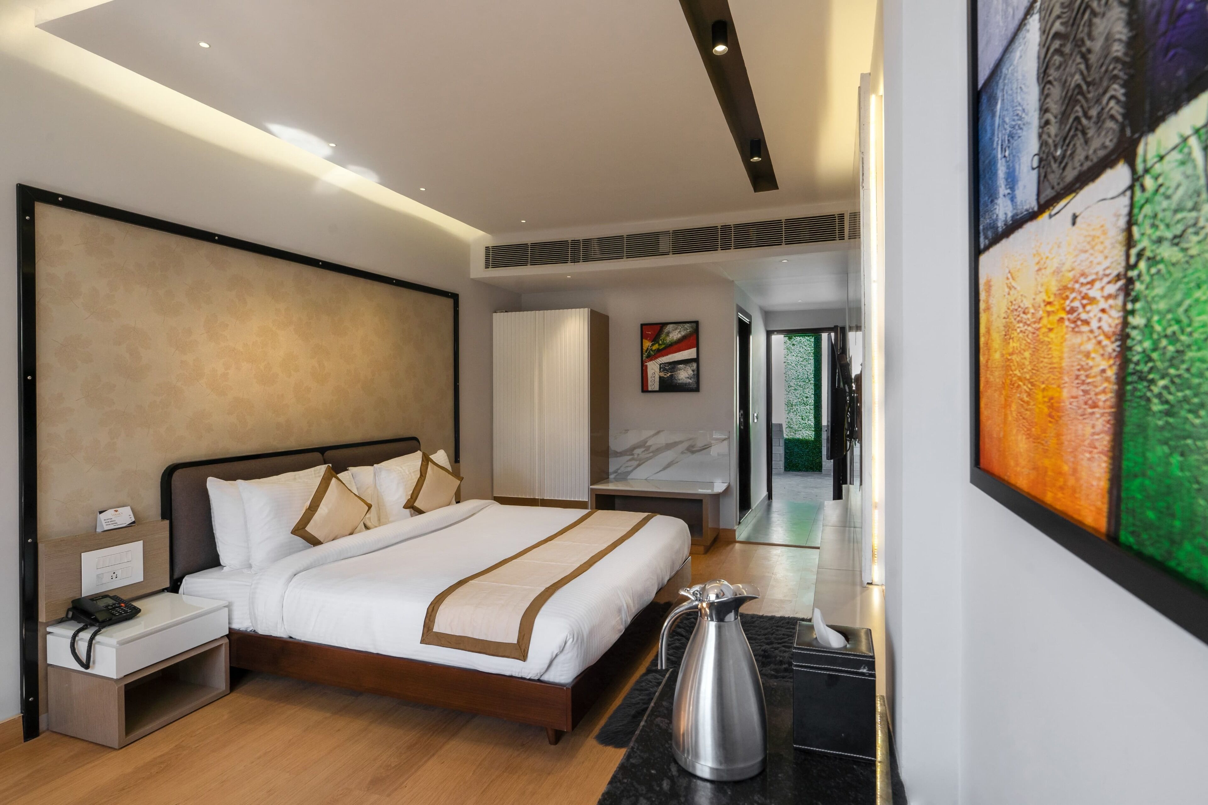 Ein modernes Hotelzimmer mit einem großen Bett, Nachttischen, einem Beistelltisch, einem an der Wand montierten Telefon, einer dekorativen Karaffe und einem großen abstrakten Gemälde.