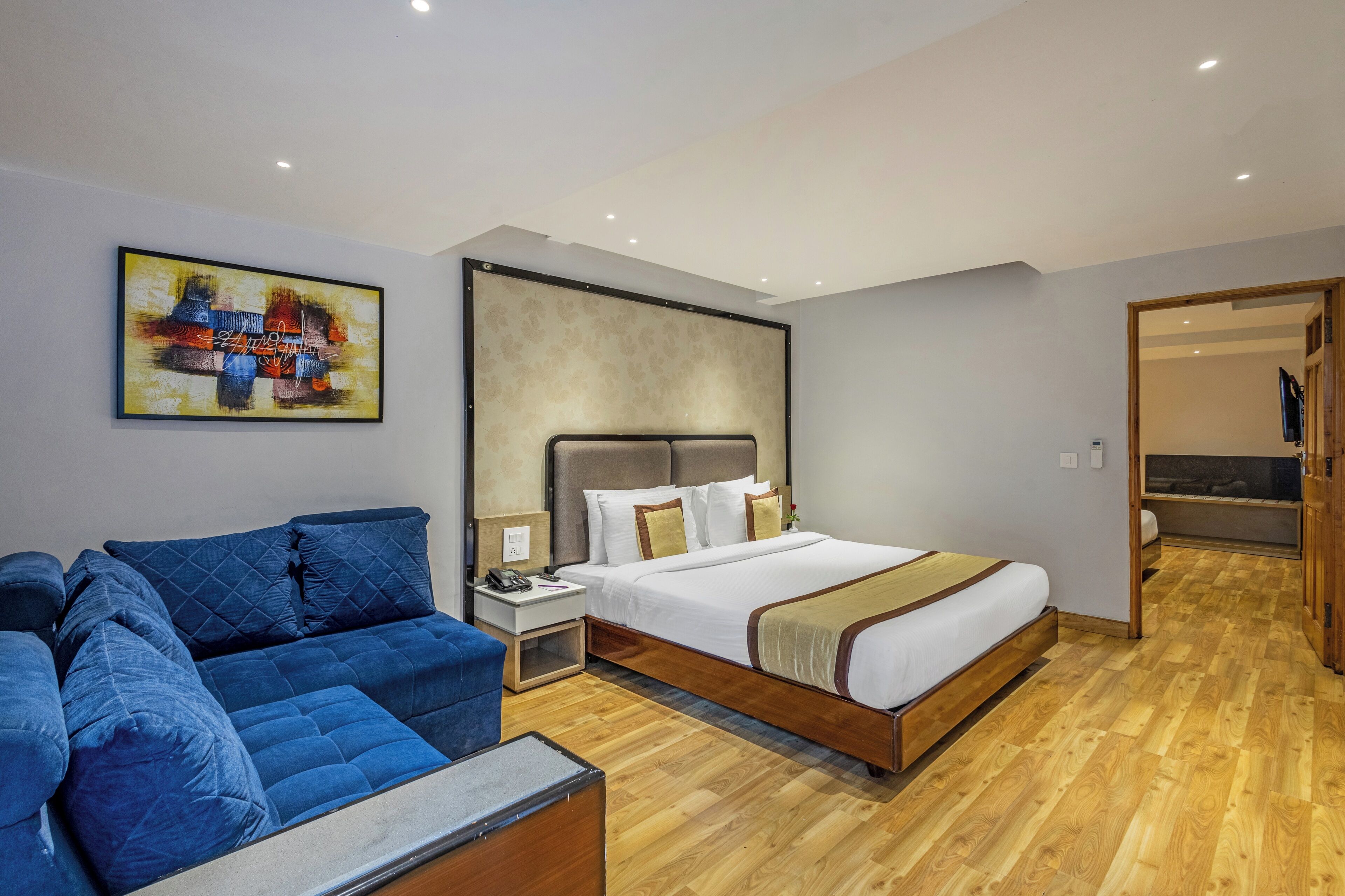 A modern hotel room with a large bed, a blue sofa, and a wooden floor.