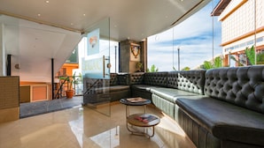 A modern lounge area with a leather sofa, a small round table, and a glass partition. - The Legacy Luxury By Bridge View (Shimla)