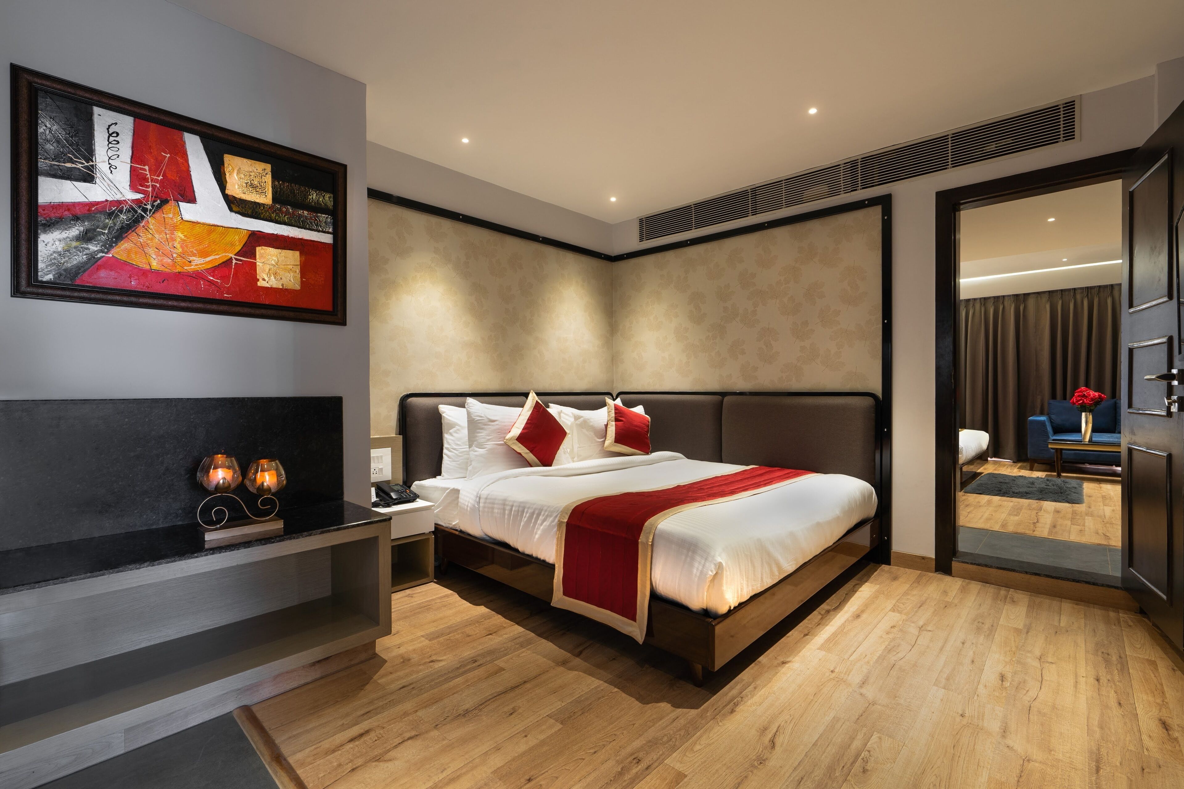 Ein modernes Hotelzimmer mit einem großen Bett, einem Nachttisch, einem Wandbild und Blick in das angrenzende Zimmer.