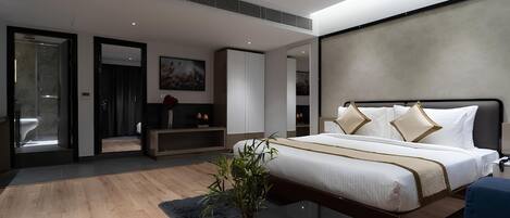 A modern hotel room with a large bed, a bedside table, a desk, and a seating area with a sofa.