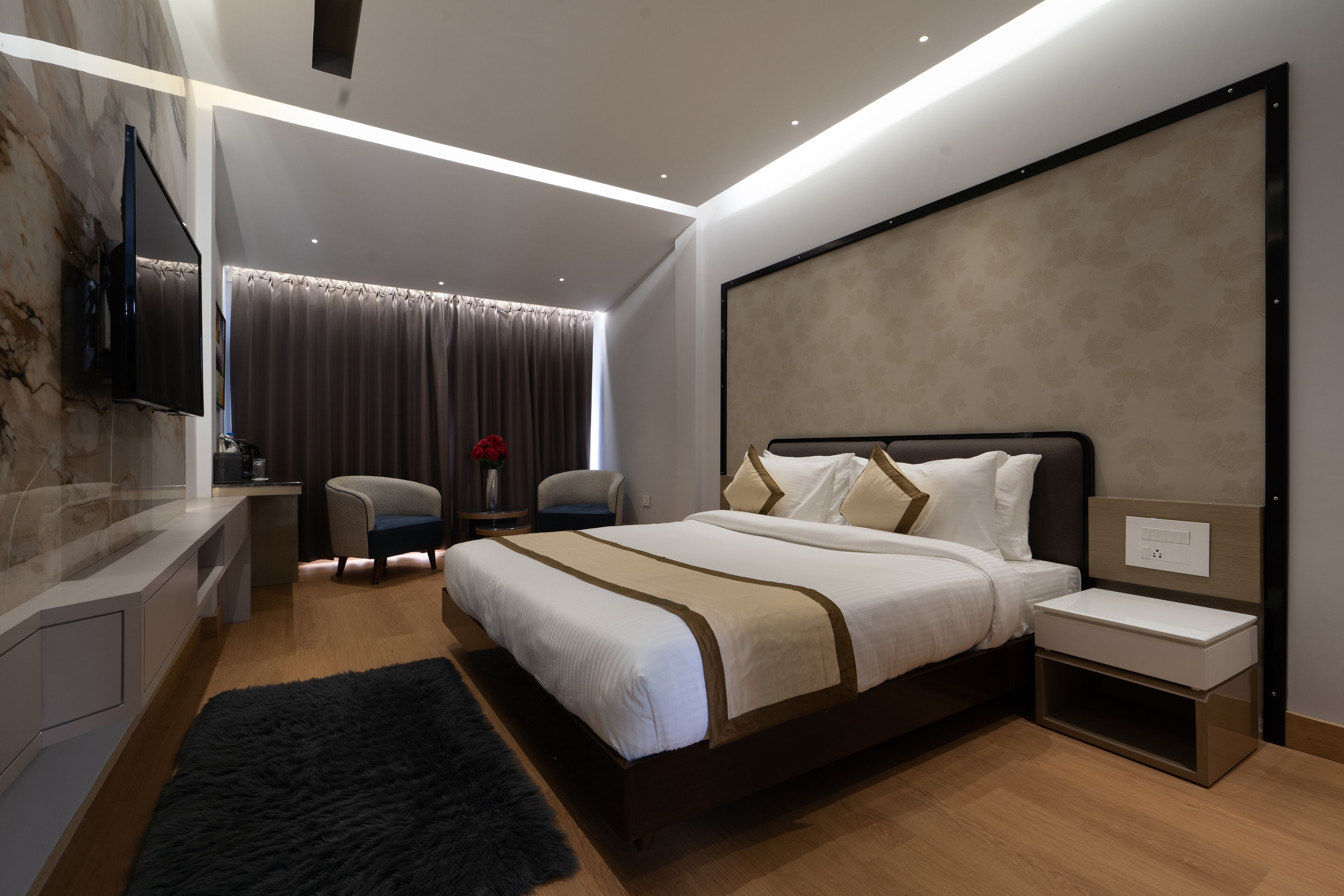 A modern bedroom with a large bed, bedside tables, a TV mounted on the wall, and a desk with a chair.