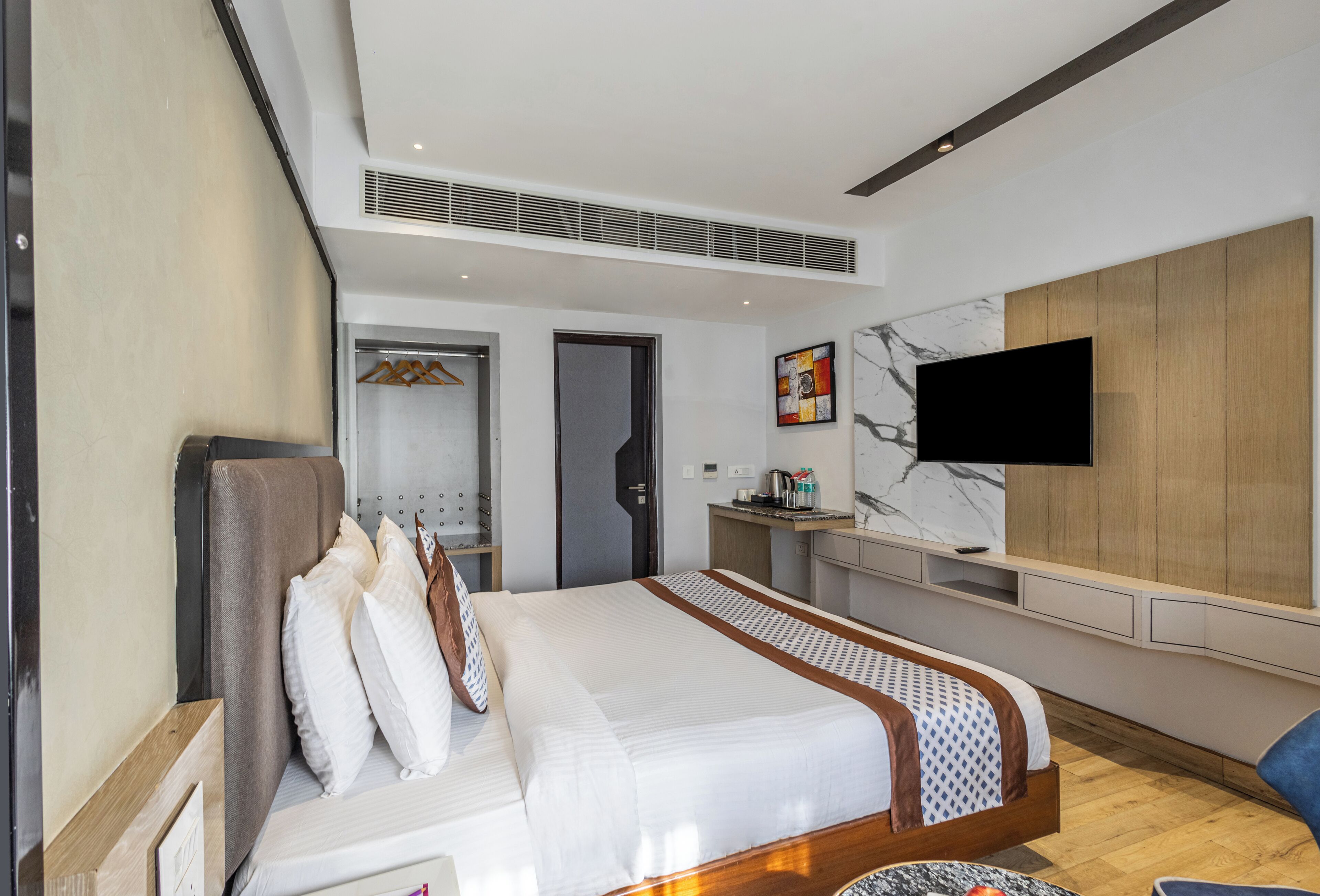 A modern hotel room with a large bed, a TV mounted on the wall, a desk, and a wardrobe.