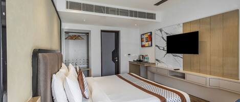 A modern hotel room with a large bed, a TV mounted on the wall, a desk, and a wardrobe.