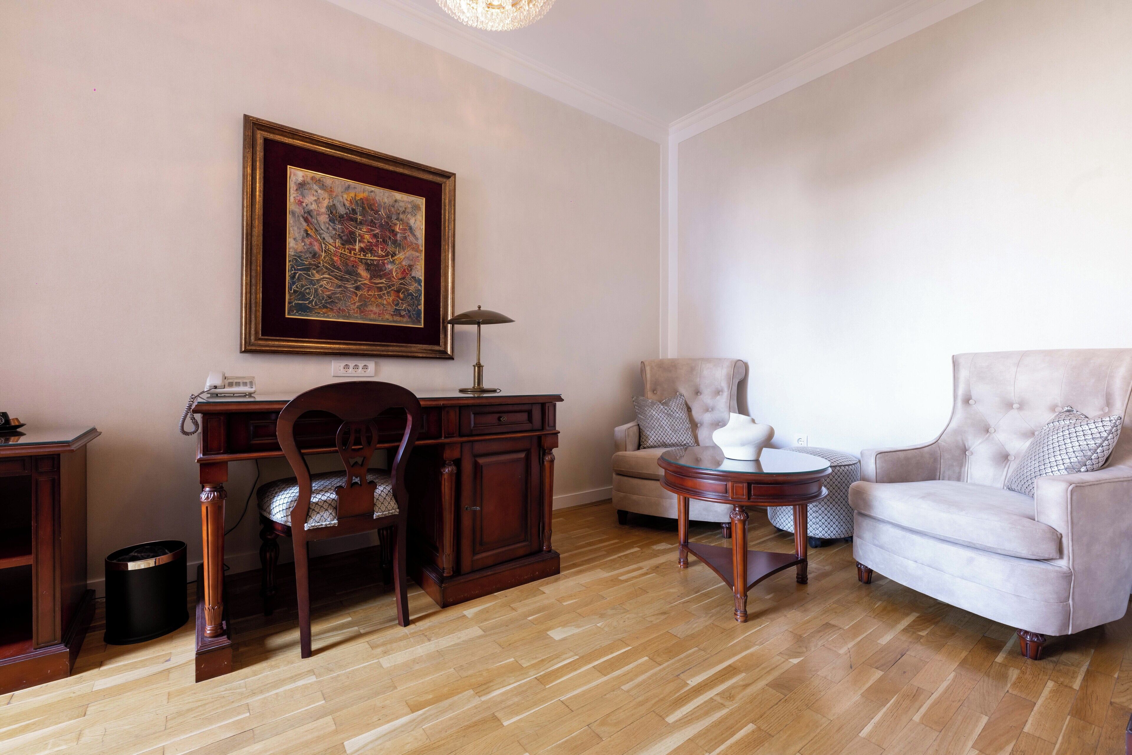 Een woonkamer met een houten bureau, een stoel, een bank en een lijst met een schilderij aan de muur.