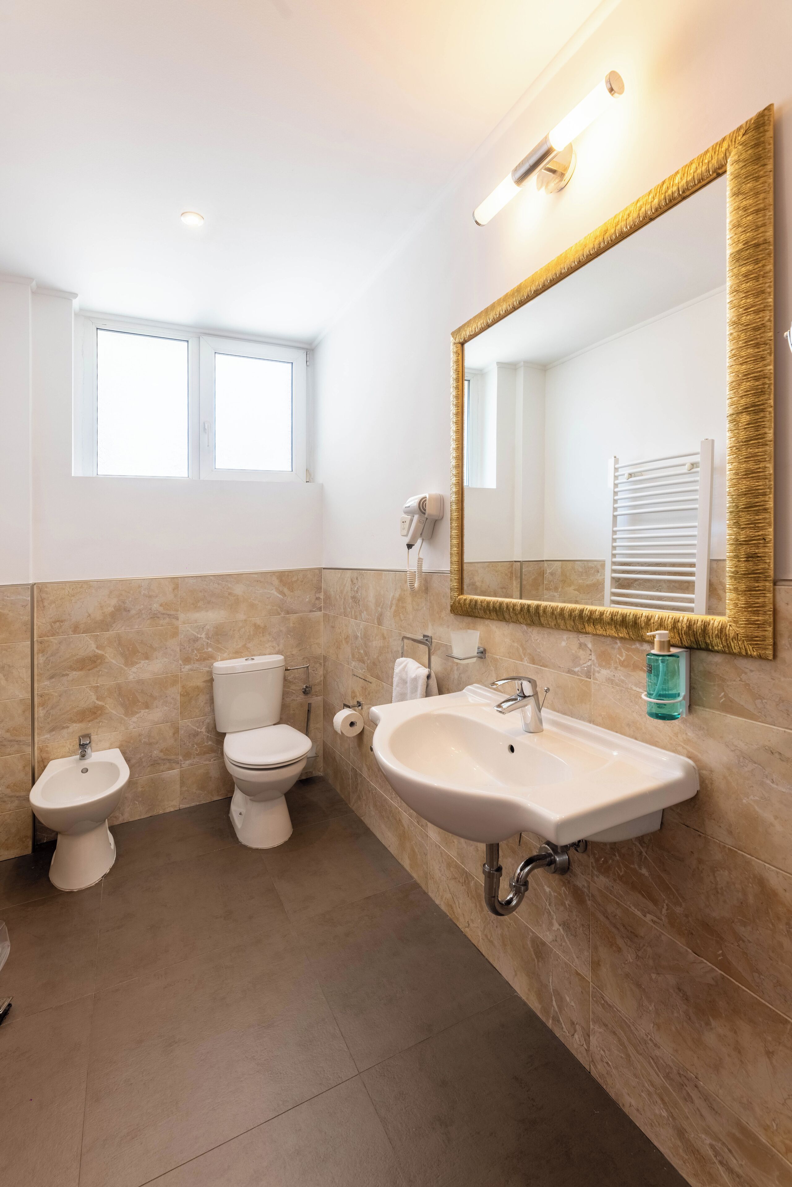 A bathroom with a large mirror, a sink, two toilets, and a window.